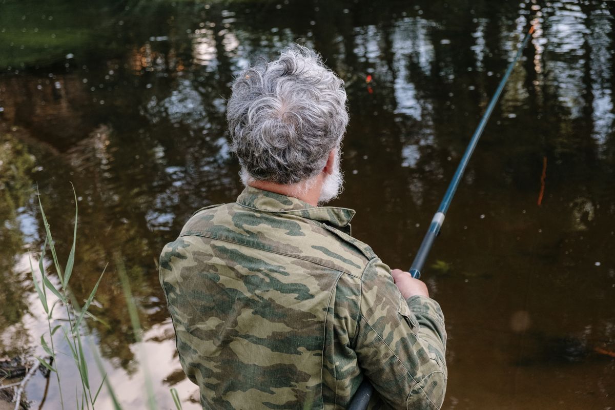 A grey-haired man fishing by a lake — retirement gift ideas for men